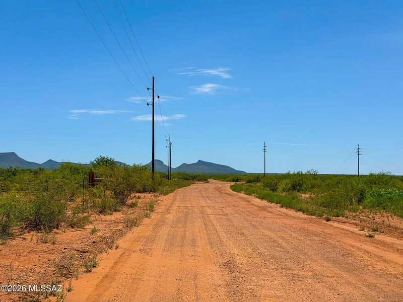 Graded red dirt road running past the parcels with power poles along it and mountains in the distance