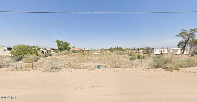 Street view of the flat vacant lot with neighboring homes and an overhead wire across the top of the frame