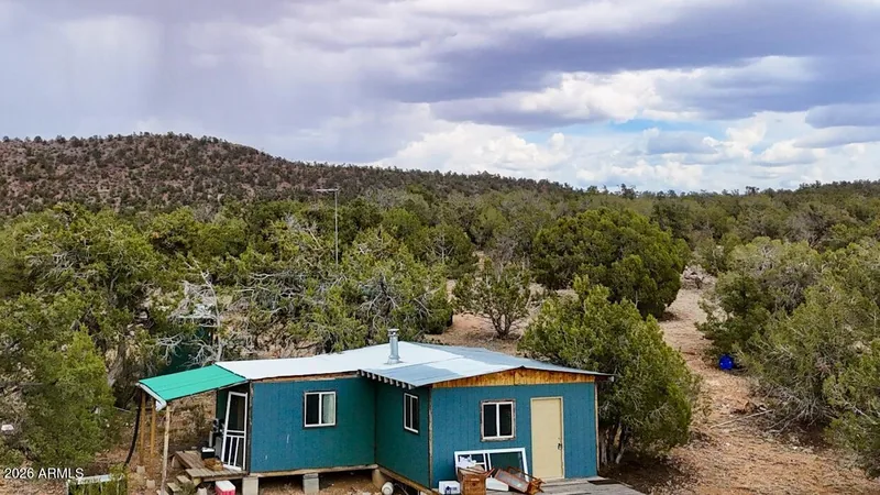 Teal off-grid cabin with a covered porch among junipers on the 5 acres, seen from above