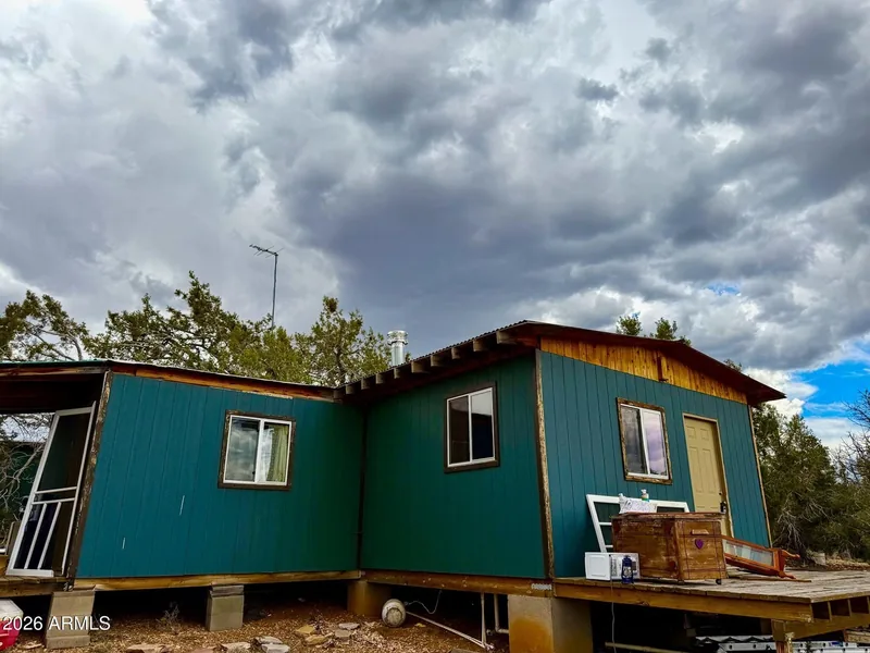 Rear of the teal cabin with windows and a wood-frame deck under storm clouds