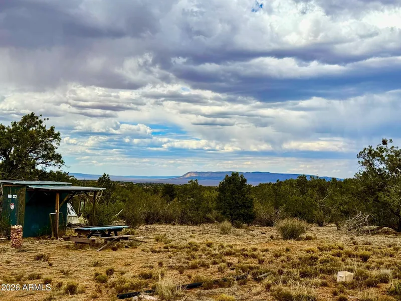 The cabin and a picnic table among junipers with the wide valley and distant mesas beyond