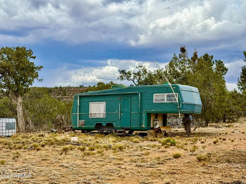 Green fifth-wheel trailer parked among the junipers on the property