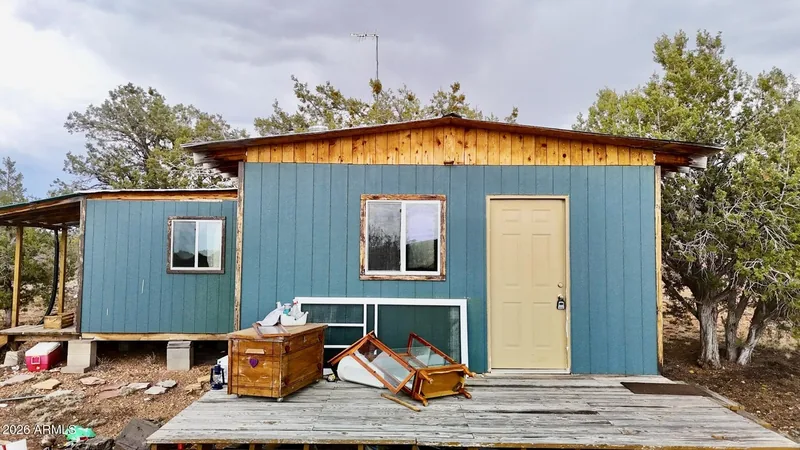 Front of the teal cabin with its door, windows and a wood deck with building materials