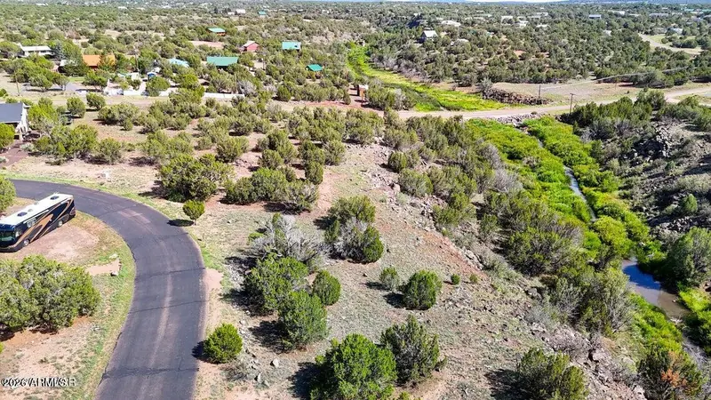 Aerial view of paved Creekside Circle winding past homes and the creek bottom among junipers